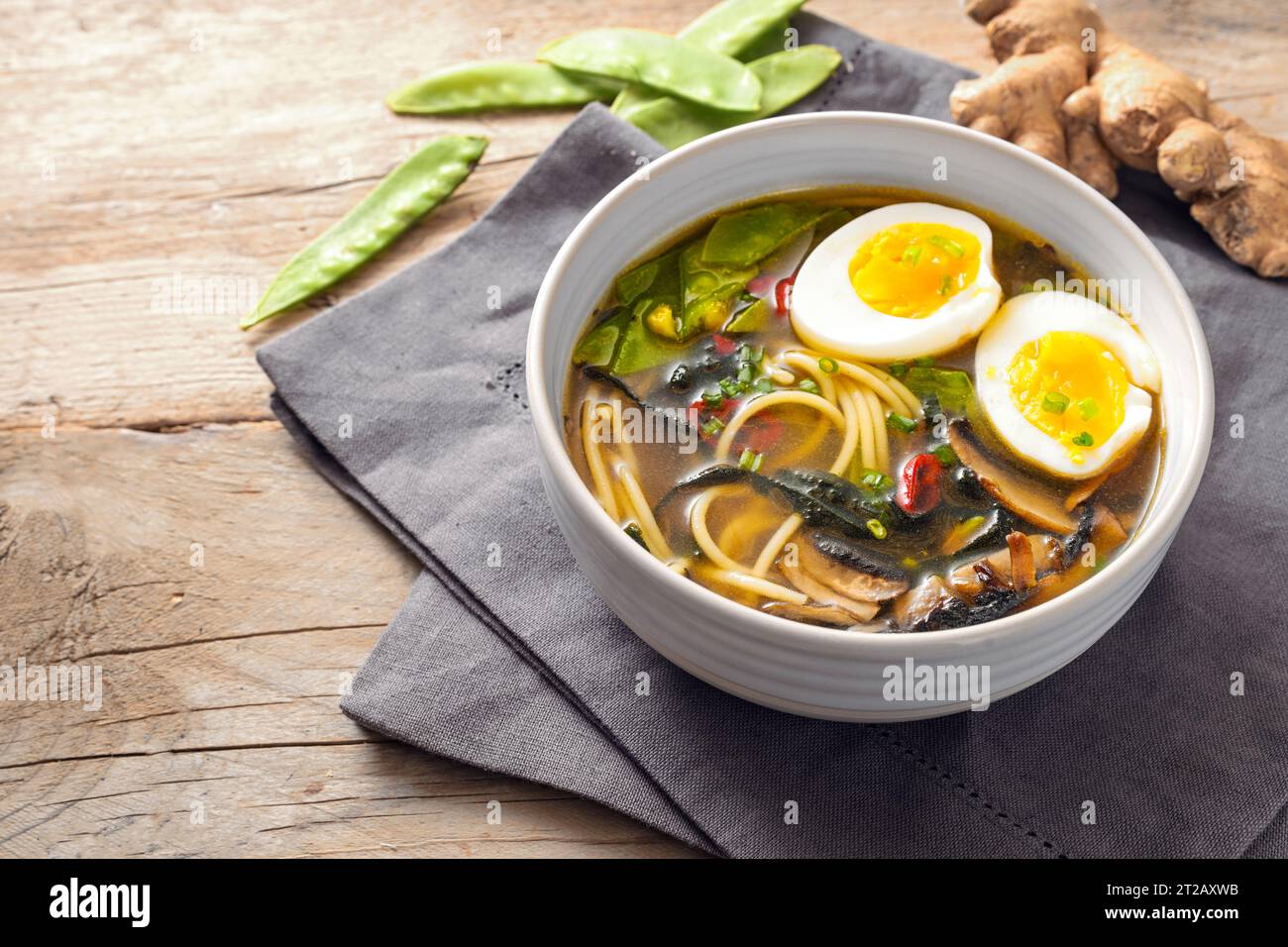 Zuppa di miso con spaghetti, alghe nori, piselli da neve, zenzero e uovo in una ciotola su un tavolo rustico in legno, spazio per copiare, messa a fuoco selezionata, profondità ridotta di fie Foto Stock