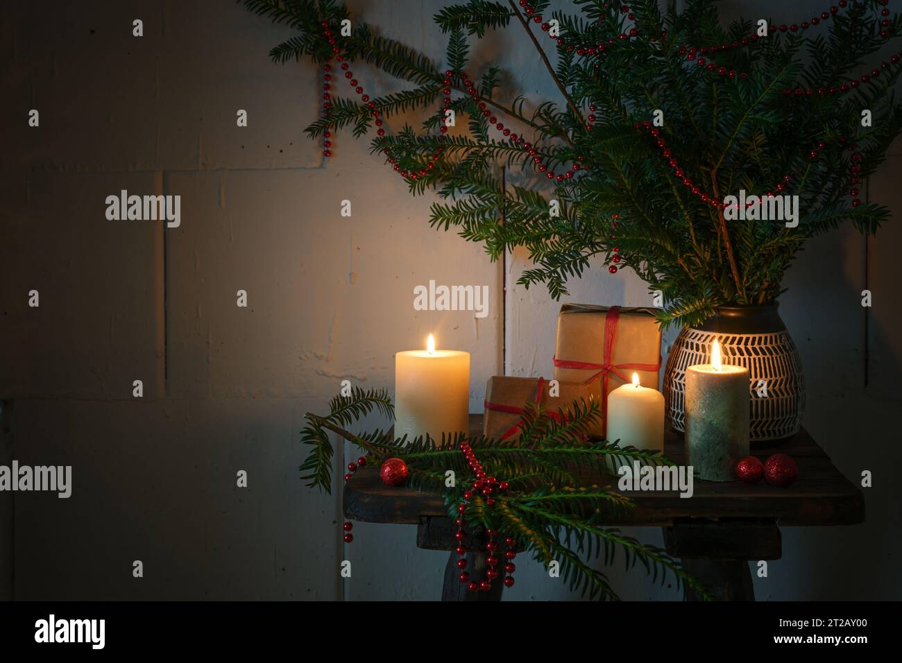 Natale con candele in fiamme, regali, rami sempreverdi e decorazioni su un piccolo tavolo di legno, luce calda e accogliente nella stagione buia, spazio fotocopie, Foto Stock