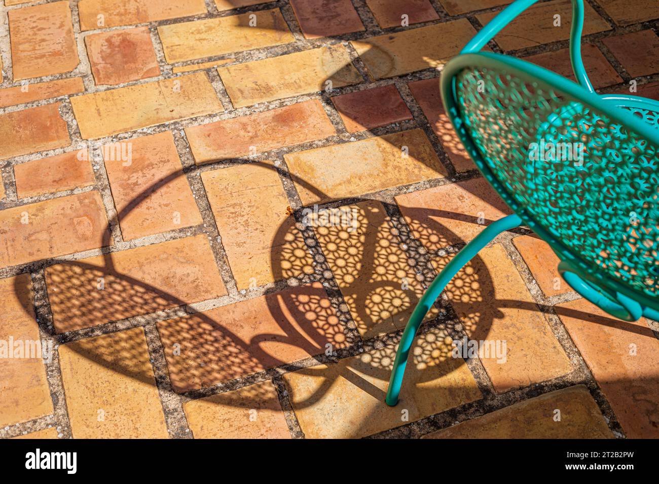 Sedia in ferro decorata in ottanio e la sua ombra si riflette su un pavimento in mattoni rustici in estate Foto Stock