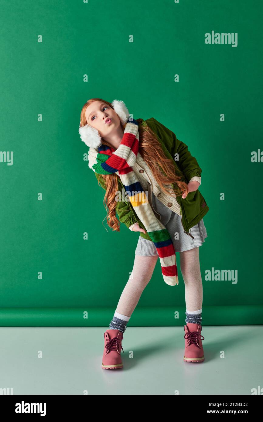 a tutta lunghezza, ragazza preadolescente con cuffie, sciarpa a righe e outfit invernale con labbra turchesi Foto Stock