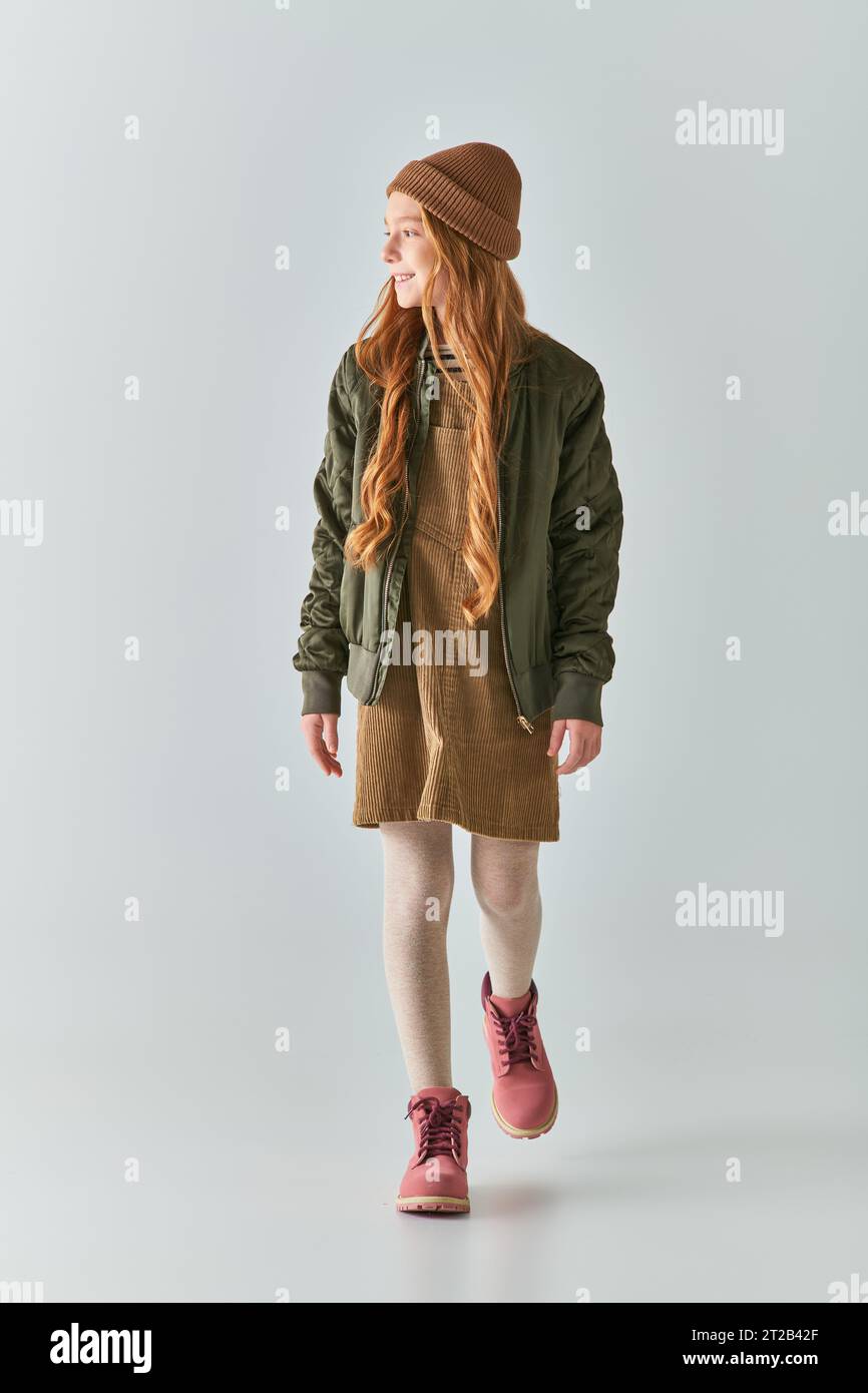felice preadolescente con i capelli lunghi che cammina in inverno, cappello, giacca sopra l'abito e stivali grigi Foto Stock