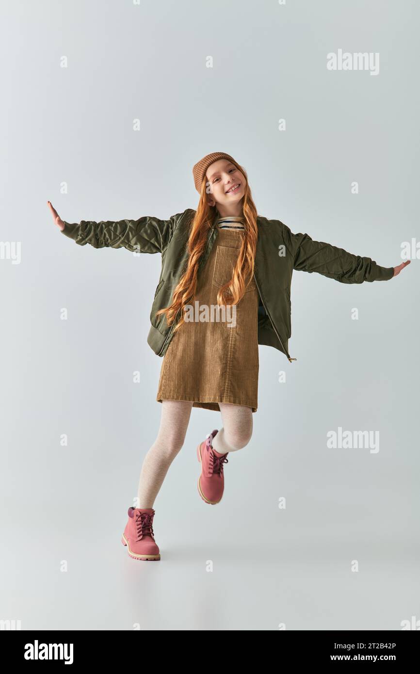 happy girl completa in outfit invernale e cappello in maglia con le mani allungate sul grigio Foto Stock