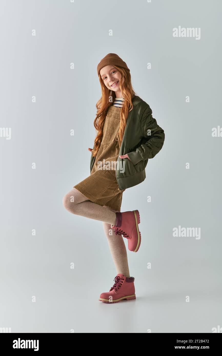 moda invernale, ragazza gioiosa con capelli lunghi e cappello in maglia in abito e giacca grigia Foto Stock