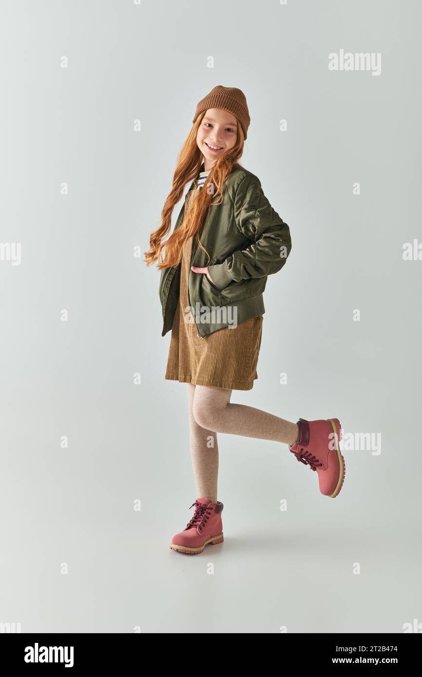 moda per bambini, ragazza felice con capelli lunghi e cappello invernale in testa in abito e giacca Foto Stock