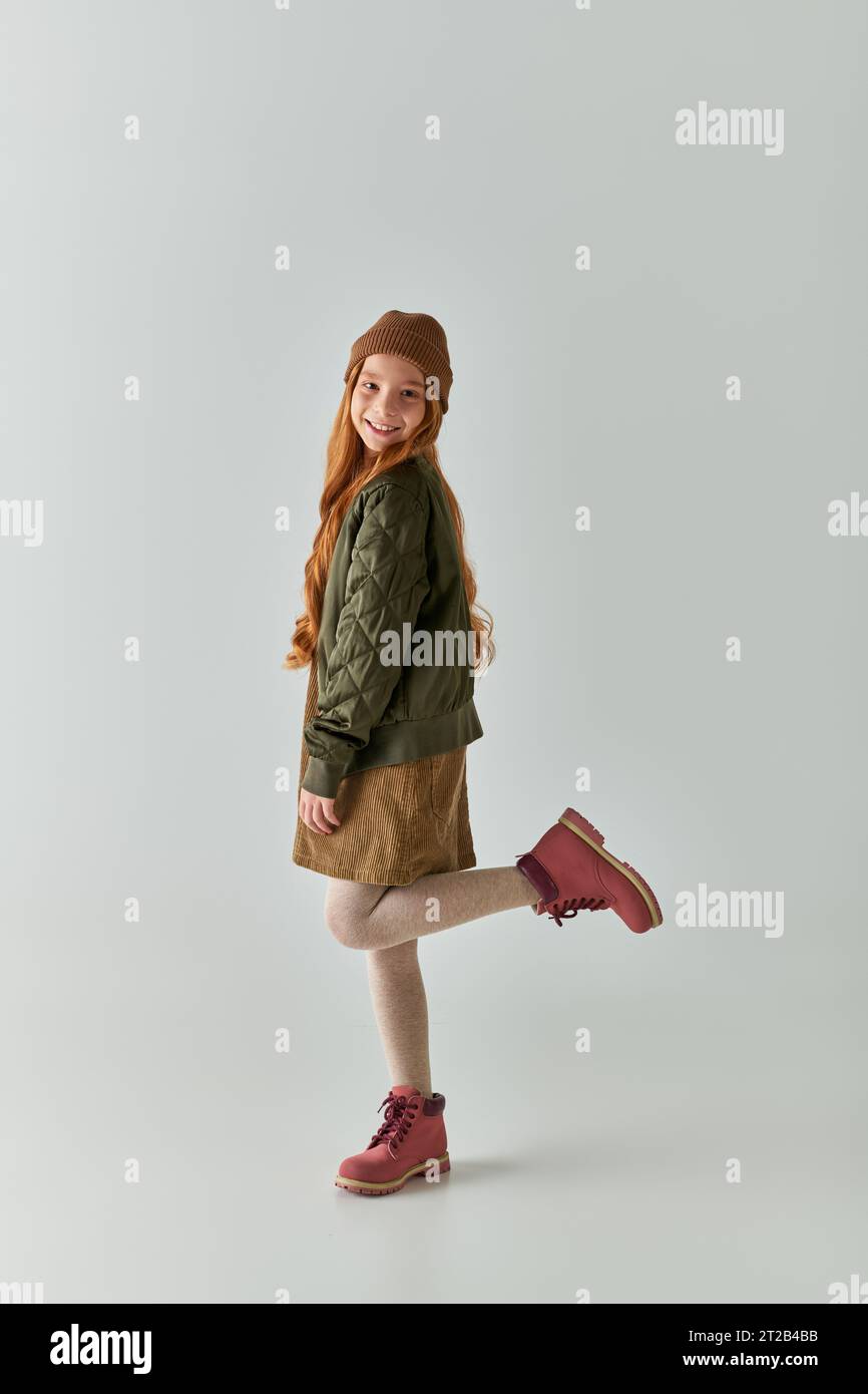 una graziosa preadolescente con lunghi capelli in abiti invernali alla moda su sfondo grigio Foto Stock