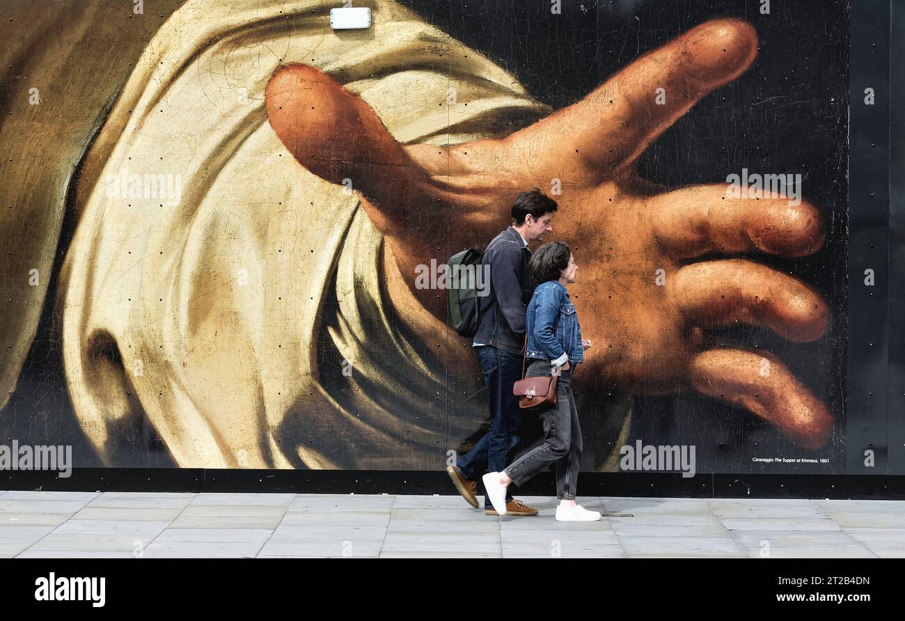 I pedoni camminano davanti a una grande riproduzione di un dipinto di Caravaggio raffigurante una grande mano di presa, su un tesoro nel centro di Londra, Inghilterra, Regno Unito Foto Stock