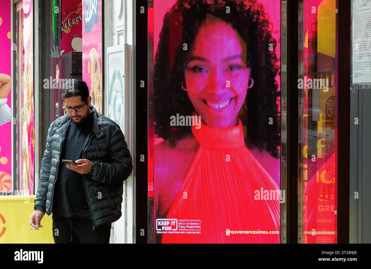 Un giovane che usa un telefono cellulare ignaro di un cartellone elettronico di una donna attraente sorridente, Central London England UK Foto Stock