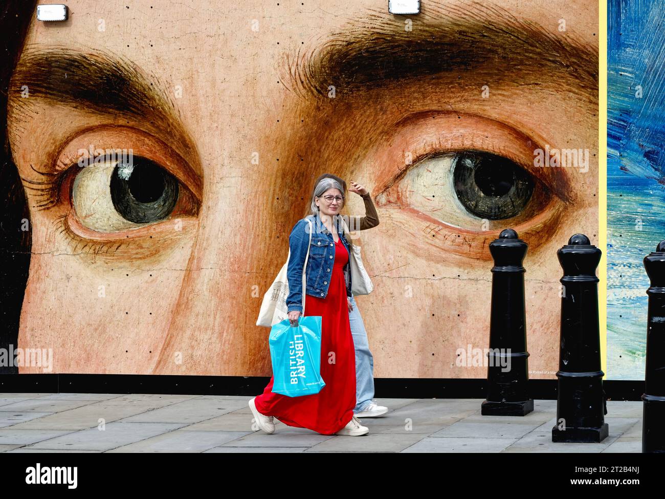 Due donne che camminano vicino a un paio di occhi da un dipinto di Antonello de Messina su un poster nel centro di Londra Inghilterra Regno Unito Foto Stock