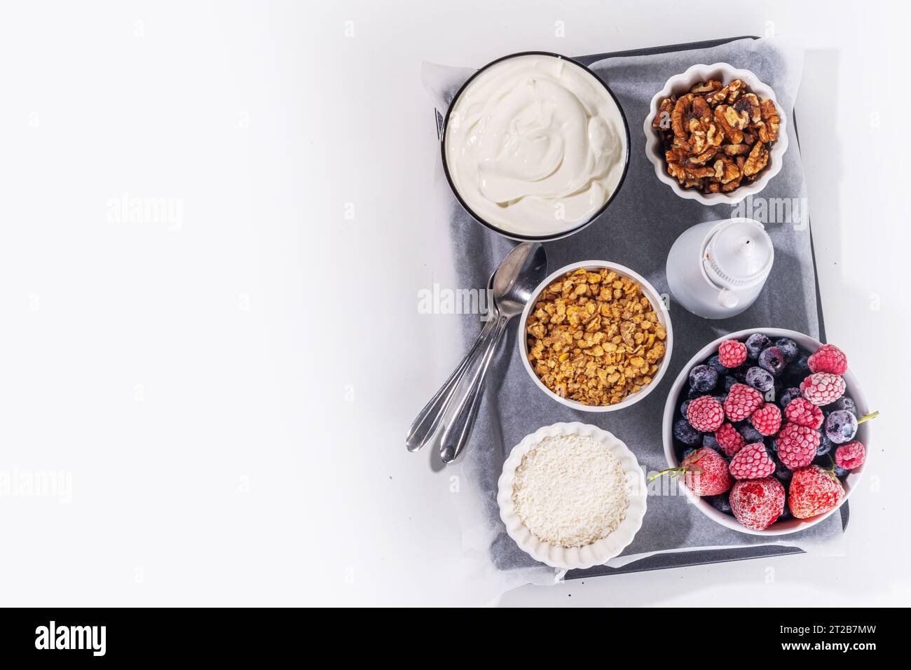 Preparazione della cottura con sfondo di corteccia di yogurt congelato con yogurt greco, bacche fresche, muesli, miele, salsa al cioccolato, con vassoio da forno deco. Vista dall'alto della donna Foto Stock