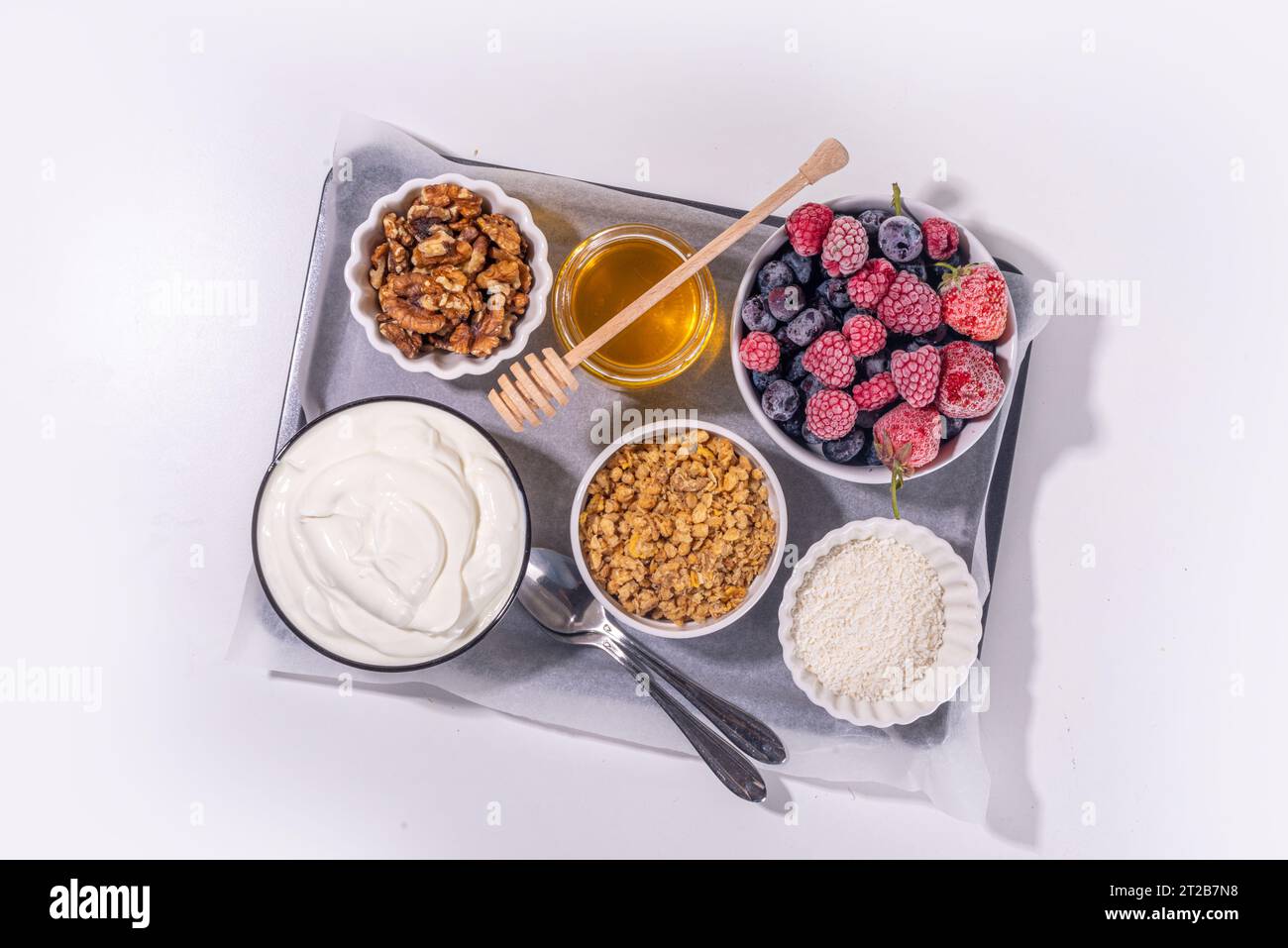 Preparazione della cottura con sfondo di corteccia di yogurt congelato con yogurt greco, bacche fresche, muesli, miele, salsa al cioccolato, con vassoio da forno deco. Vista dall'alto della donna Foto Stock