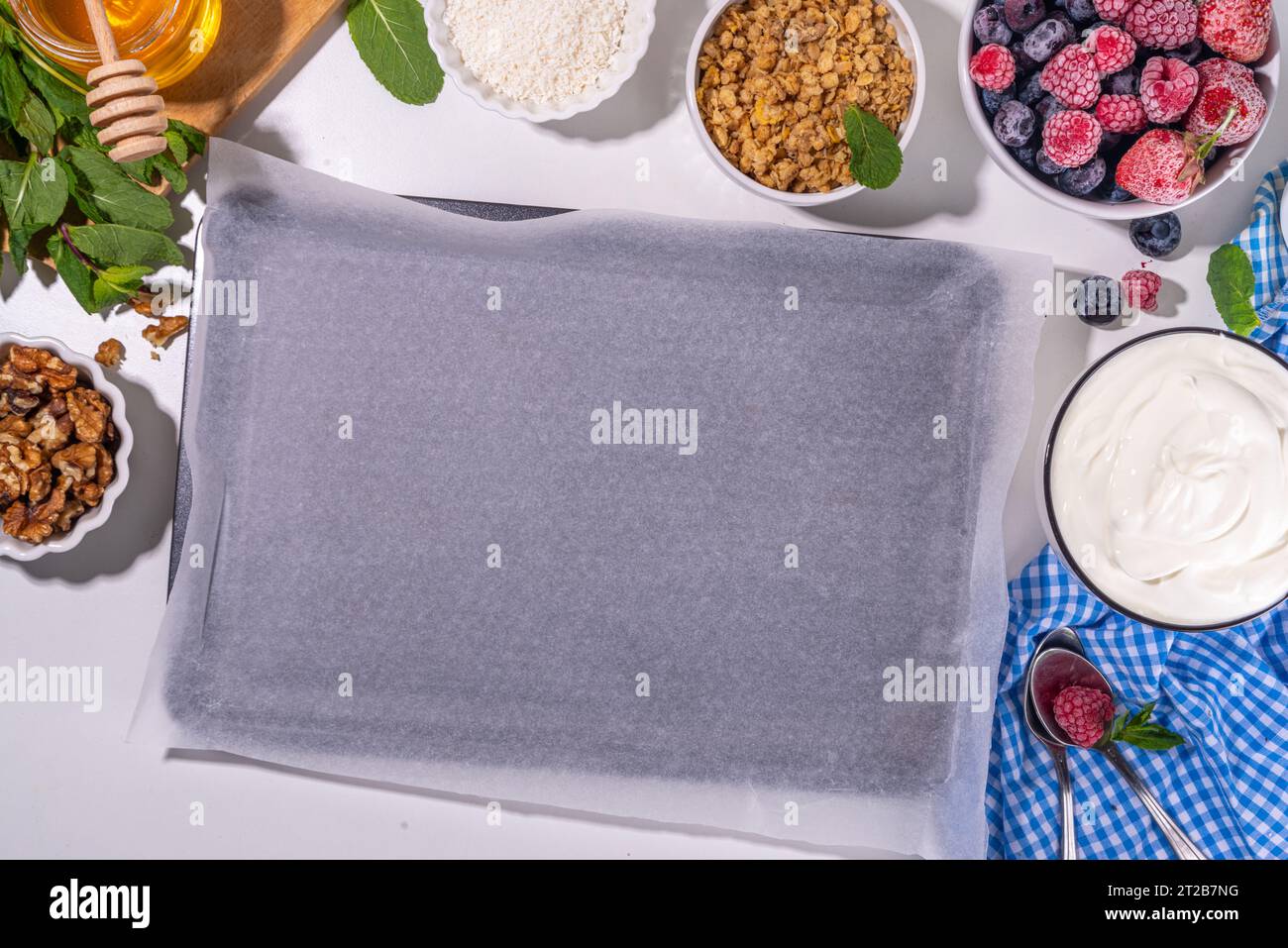 Preparazione della cottura con sfondo di corteccia di yogurt congelato con yogurt greco, bacche fresche, muesli, miele, salsa al cioccolato, con vassoio da forno deco. Vista dall'alto della donna Foto Stock