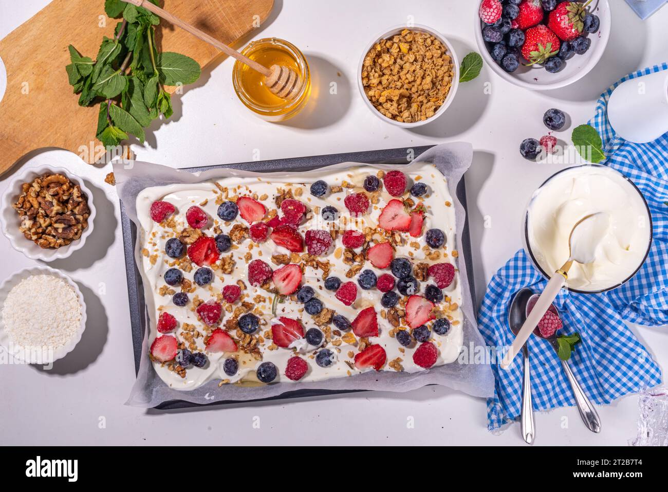 Preparazione della cottura con sfondo di corteccia di yogurt congelato con yogurt greco, bacche fresche, muesli, miele, salsa al cioccolato, con vassoio da forno deco. Vista dall'alto della donna Foto Stock
