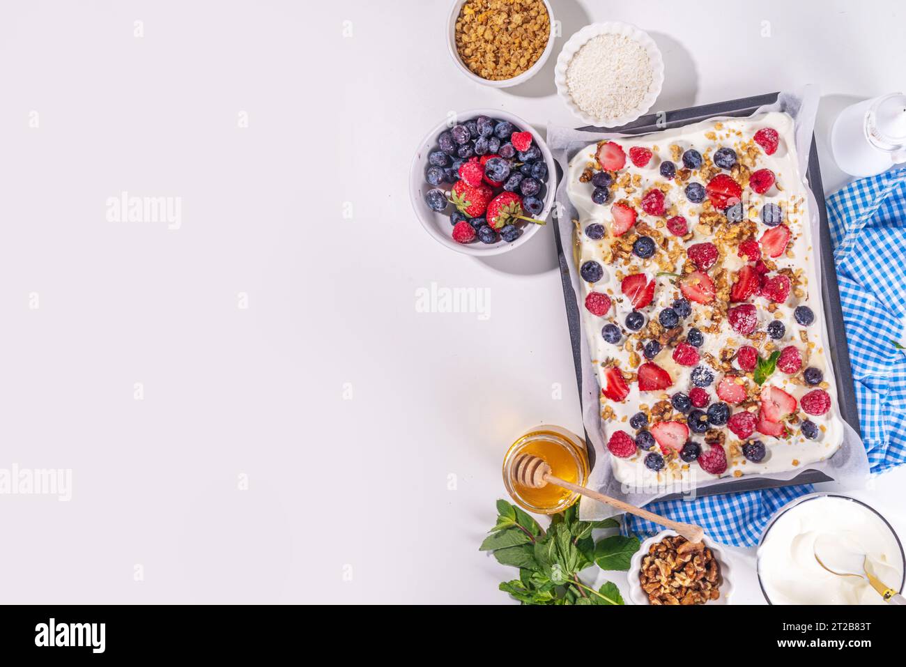 Preparazione della cottura con sfondo di corteccia di yogurt congelato con yogurt greco, bacche fresche, muesli, miele, salsa al cioccolato, con vassoio da forno deco. Vista dall'alto della donna Foto Stock