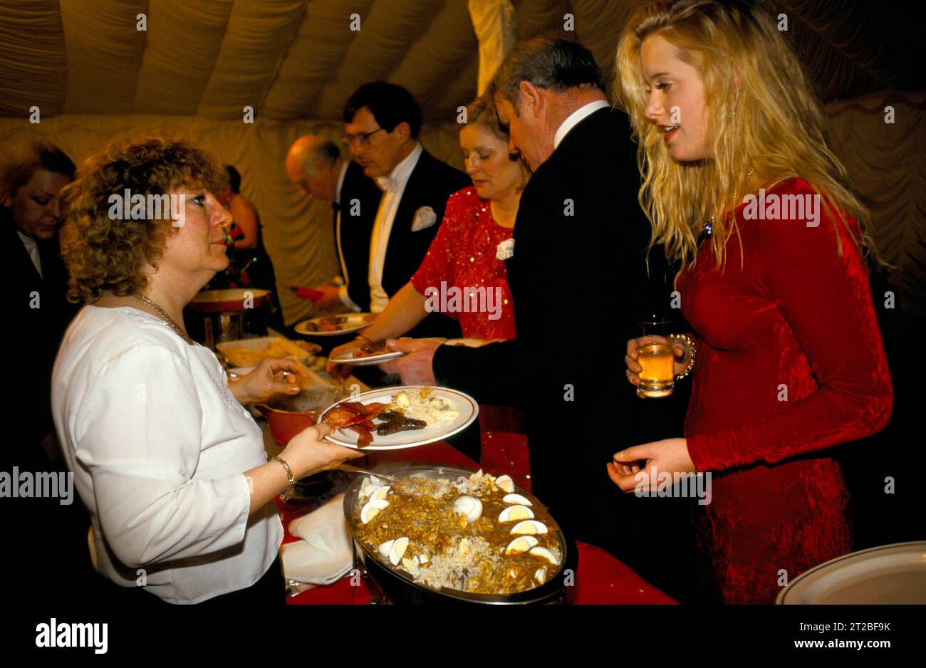 Rich Poor 1980s UK contrasto sociale classe Warwickshire Hunt Ball tenuto a Tysoe Manor. Donna che lavora part-time per una società di catering. Serve colazione, pancetta, uova, ecc. kedgeree in primo piano sul tavolo, per gli ospiti che sono stati svegli tutta la notte 1982 HOMER SYKES Foto Stock