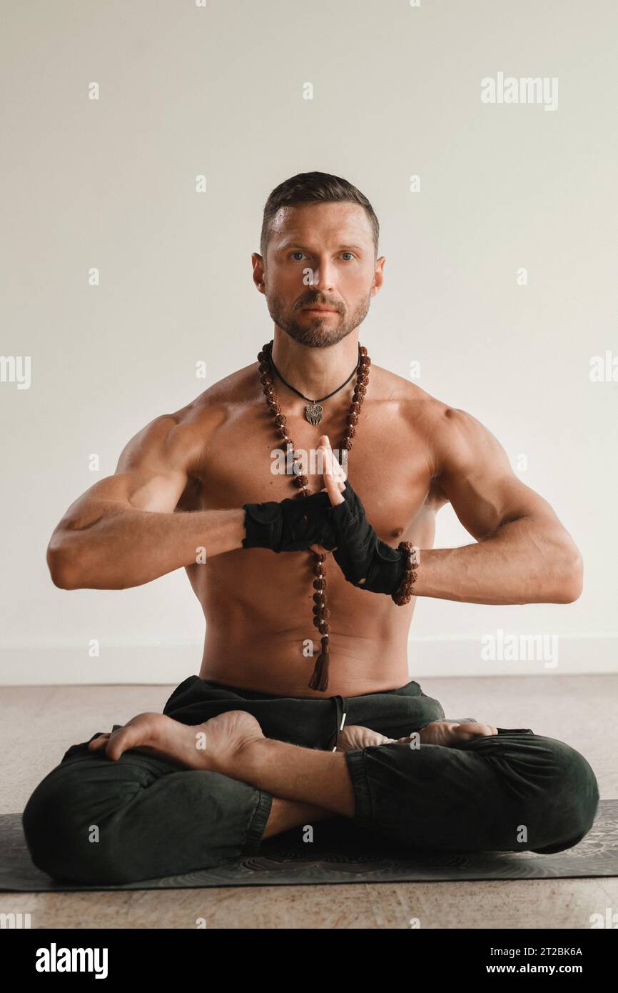 un uomo con il torso nudo è seduto in posizione di loto prima di fare yoga in casa. Fitness Trainer. Foto Stock