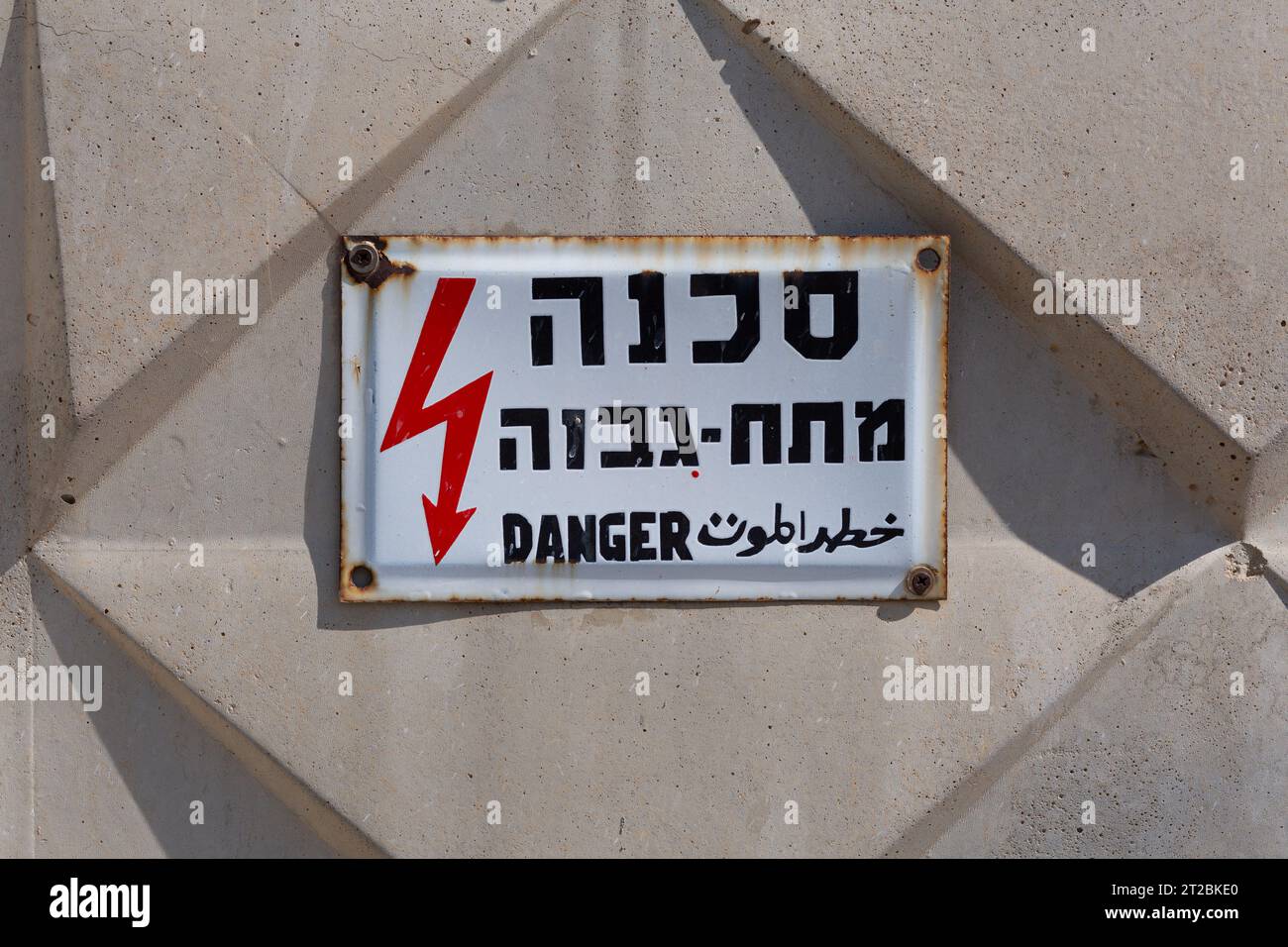 Targhetta segnaletica di pericolo per l'elettricità in ebraico, arabo e inglese, inchiodata su un muro di cemento Foto Stock