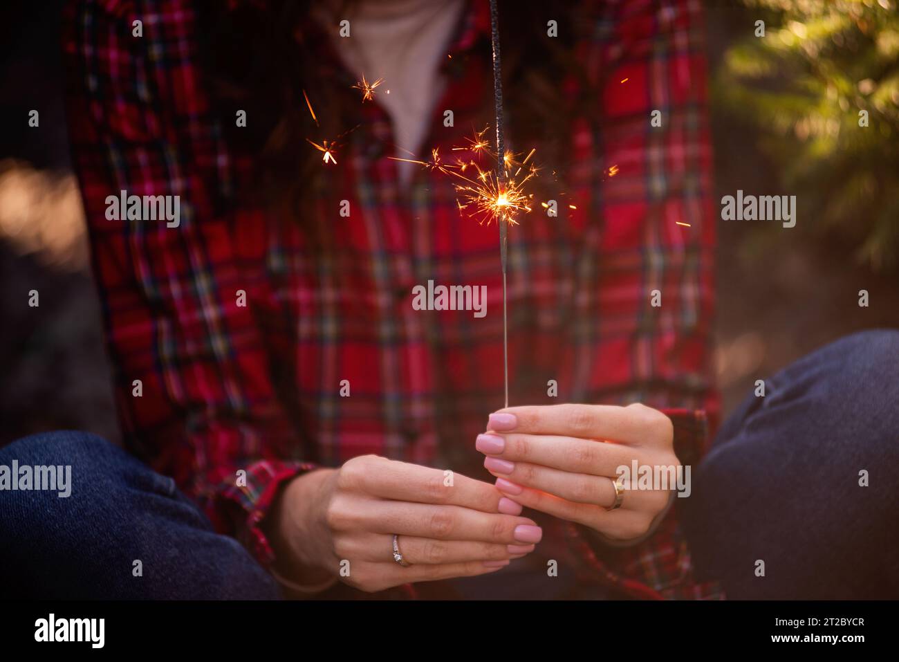 Brillante sparkler brucia nelle mani delle donne. La ragazza in camicia rossa a scacchi sorride. Atmosfera natalizia, Capodanno. Arredamento divertente per le vacanze. Foto Stock