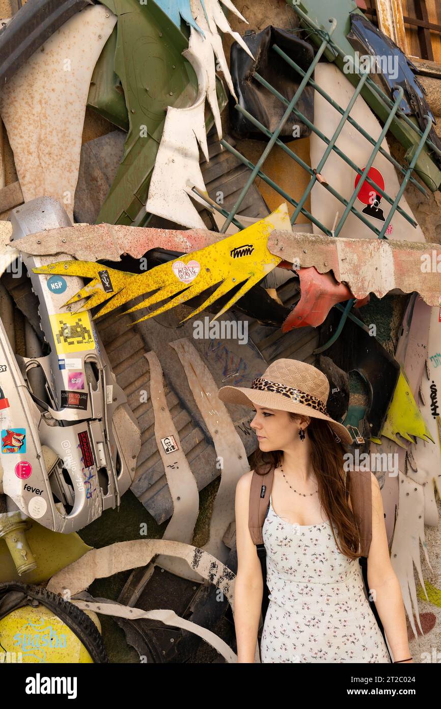 Giovane donna con un abito floreale in piedi di fronte a una pila di oggetti rotti e scartati Foto Stock