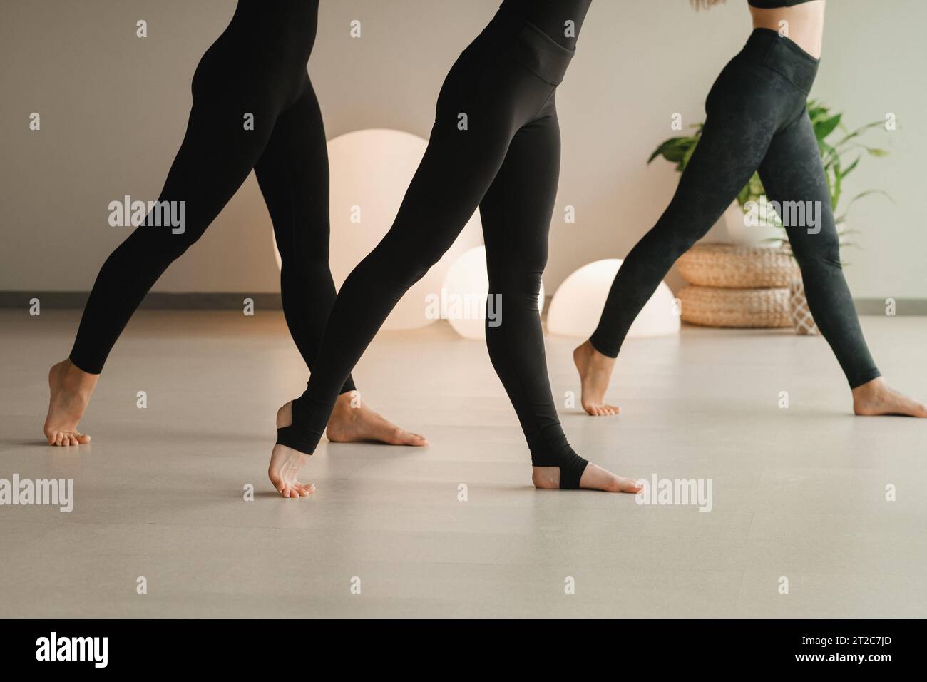 Primo piano delle gambe delle ragazze in nero che fanno yoga al chiuso. Le donne sono impegnate nel fitness. Foto Stock
