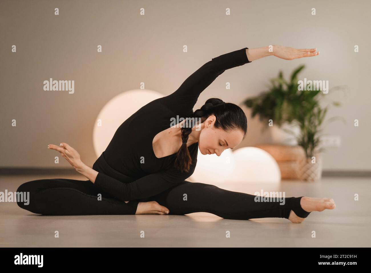 Una ragazza in abiti neri fa yoga su un tappetino al chiuso. Foto Stock