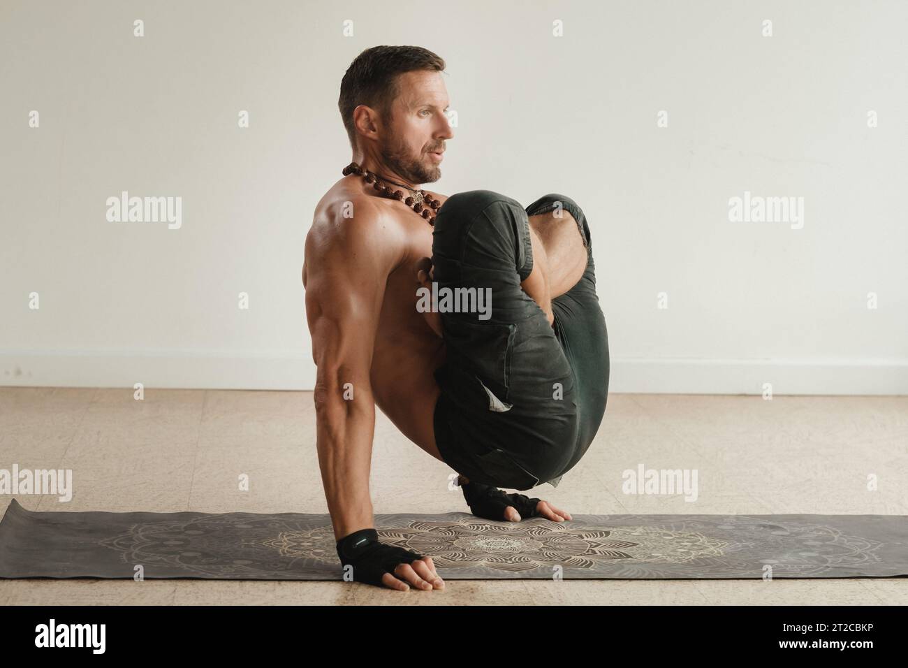 un uomo con un torso nudo fa yoga in piedi sulle mani al chiuso. Fitness Trainer. Foto Stock
