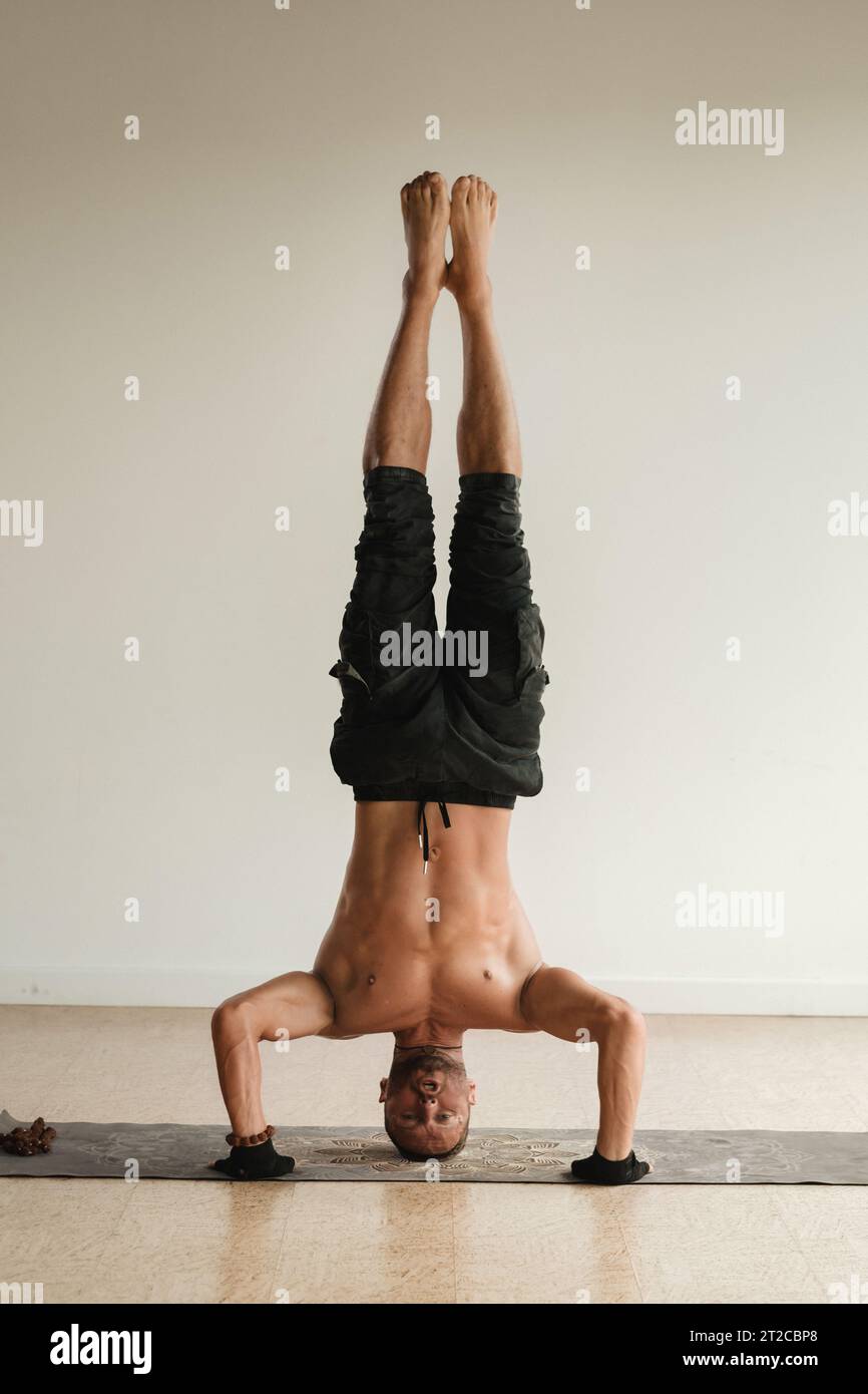 un uomo con un torso nudo fa yoga in piedi sulla testa al chiuso. Fitness Trainer. Foto Stock