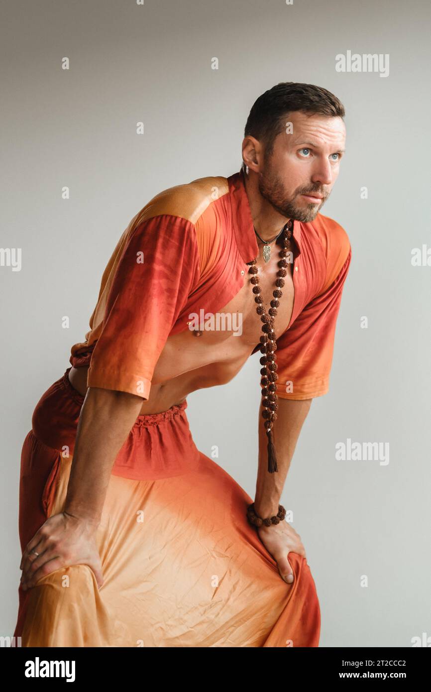 un uomo con una tuta arancione fa yoga muovendo i muscoli addominali in palestra. Il concetto di salute. Foto Stock