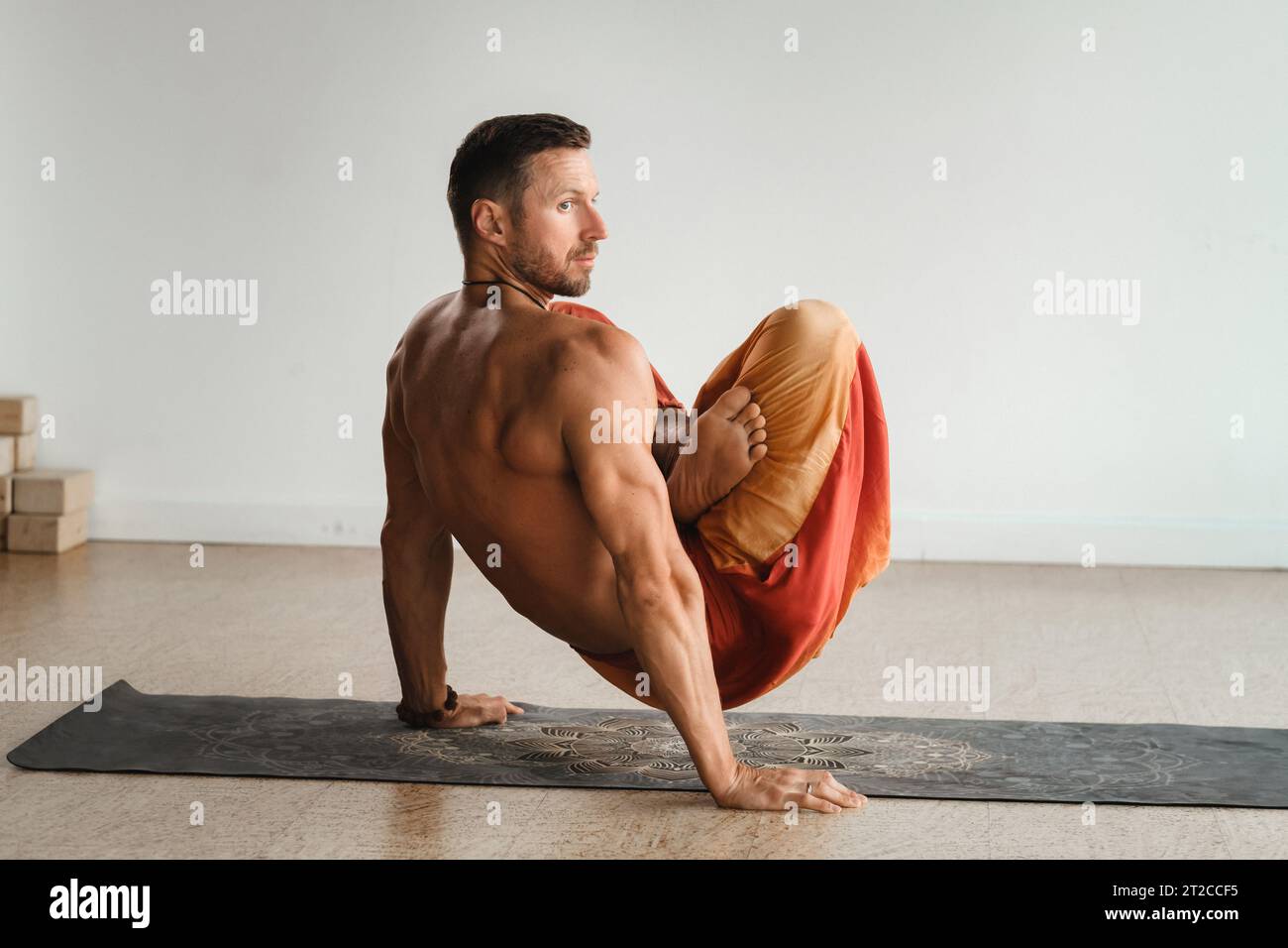 un uomo con un torso nudo fa yoga in piedi sulle mani al chiuso. Fitness Trainer. Foto Stock