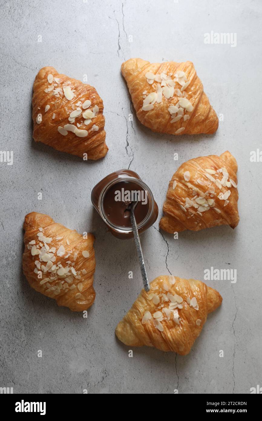 Deliziosi croissant con fiocchi di mandorle e pasta di cioccolato su tavola grigia, piatti Foto Stock