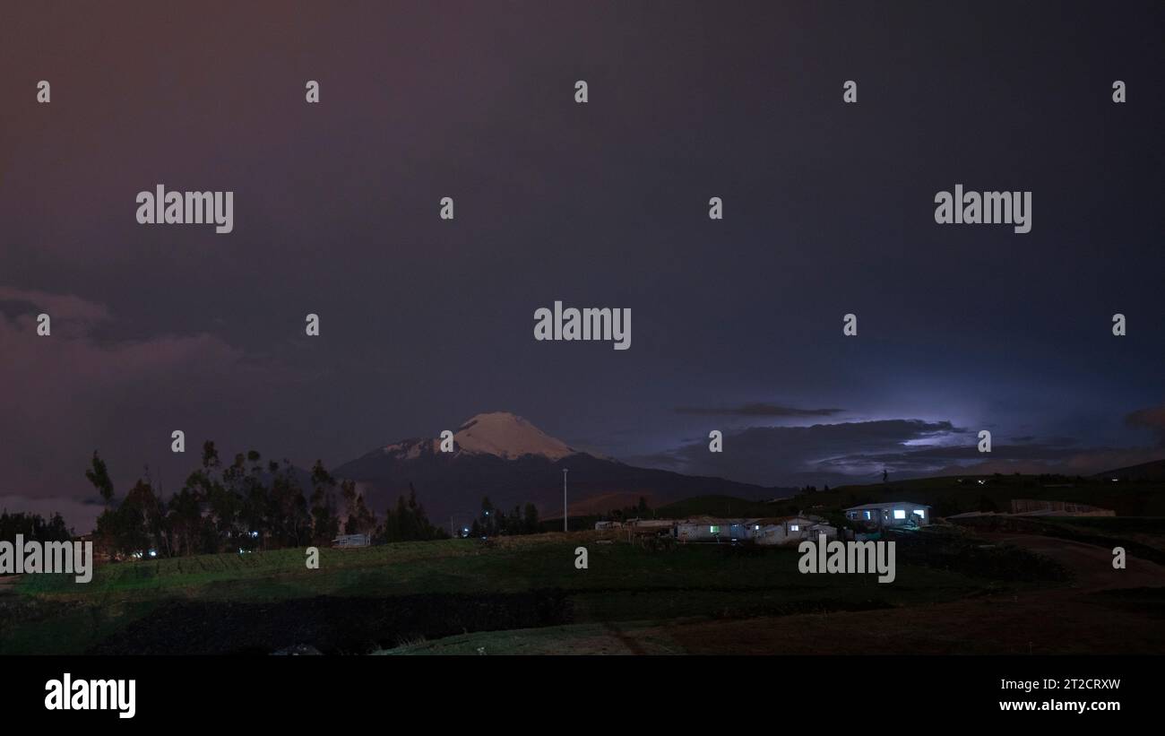 Vista notturna dal settore di Cangahua del vulcano Cayambe con cielo nuvoloso e piccole case con le luci accese Foto Stock