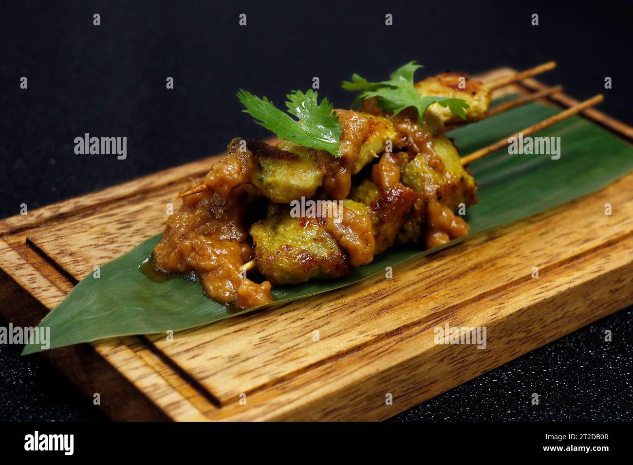 spiedino di satay di pollo indonesiano con salsa piccante di arachidi su una foglia di bambù con sfondo nero Foto Stock