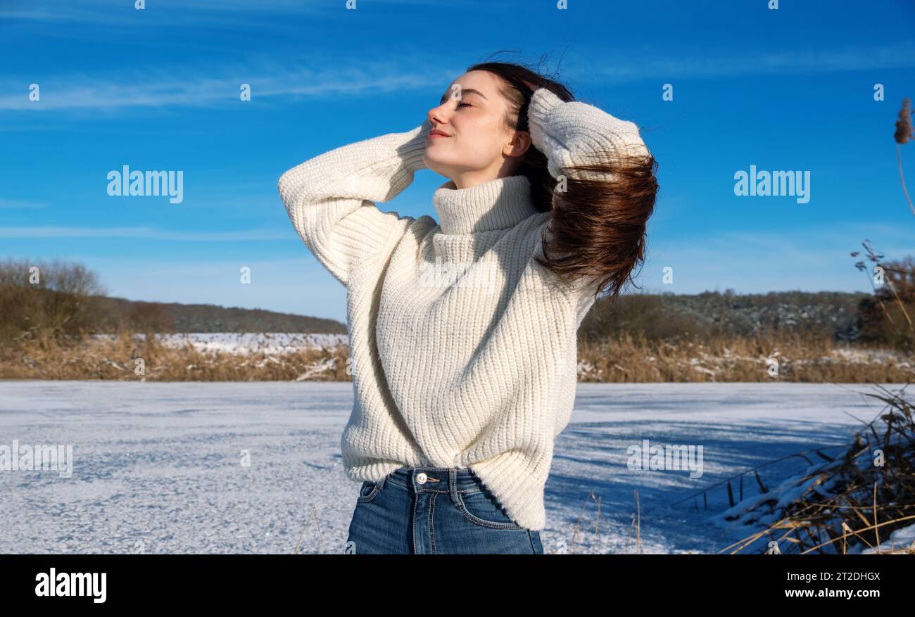 paesaggio invernale innevato di un lago ghiacciato, con una donna bruna attraente, giovane, sexy, tenendo la testa tra le mani e rilassandosi godendo la vacanza Foto Stock