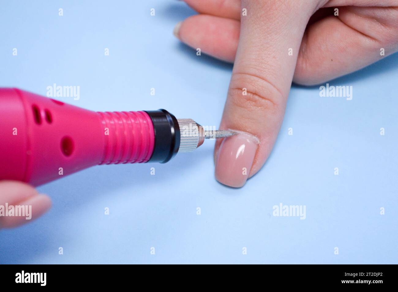 Il processo di fare una bella manicure sulle dita di un dito di lavorazione di un chiodo con una macchina speciale in un salone di bellezza unghie su un dorso blu Foto Stock