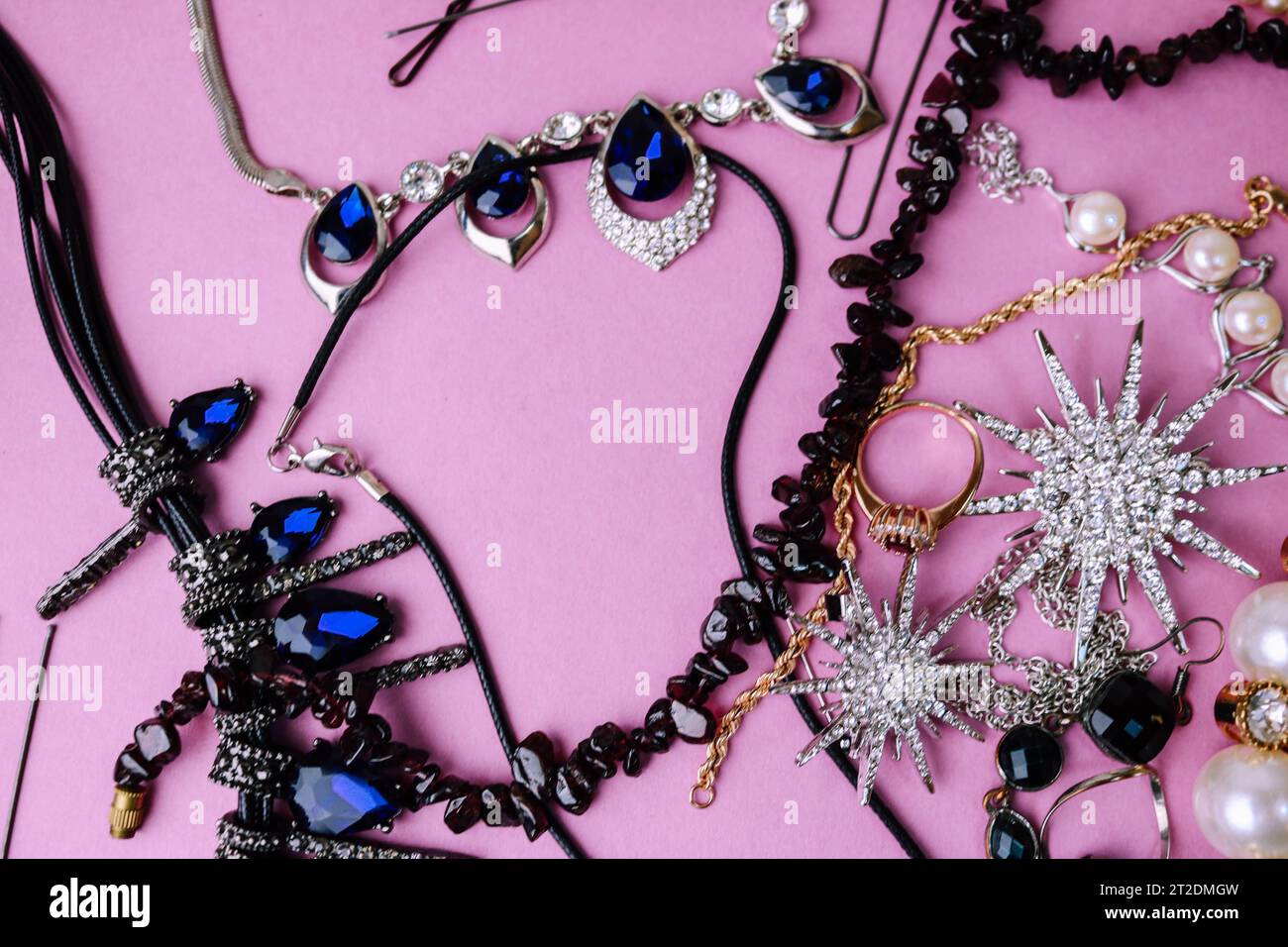 Bella gioielleria lucida e preziosa, elegante set di gioielli alla moda, collana, orecchini, anelli, catene, spilla con perle e diamanti su un viola rosa Foto Stock