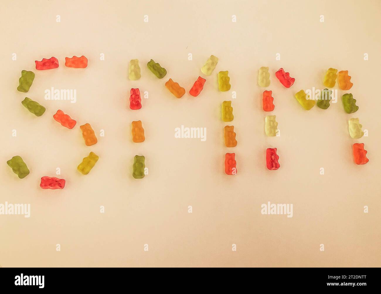 lettera di orsi gommosi multicolori. Lettere S e M realizzate con caramelle gelatinose su sfondo arancione opaco. Parola commestibile SMM. commercializzazione di gomme Foto Stock