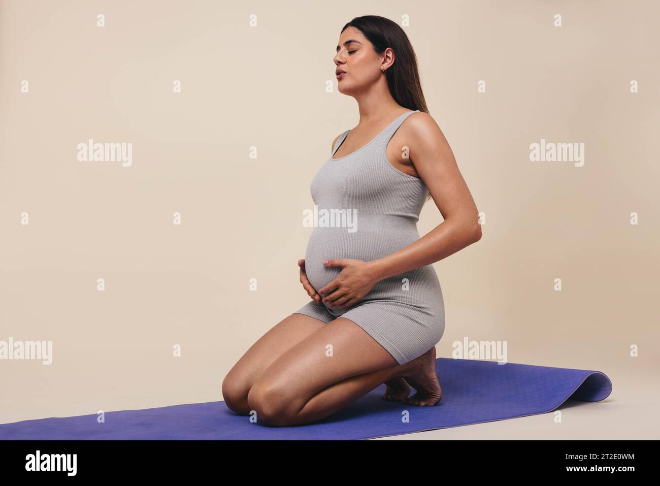 una donna incinta pratica yoga prenatale in uno studio, concentrandosi sul suo benessere durante il terzo trimestre. Indossa abiti da fitness, si allena e.. Foto Stock