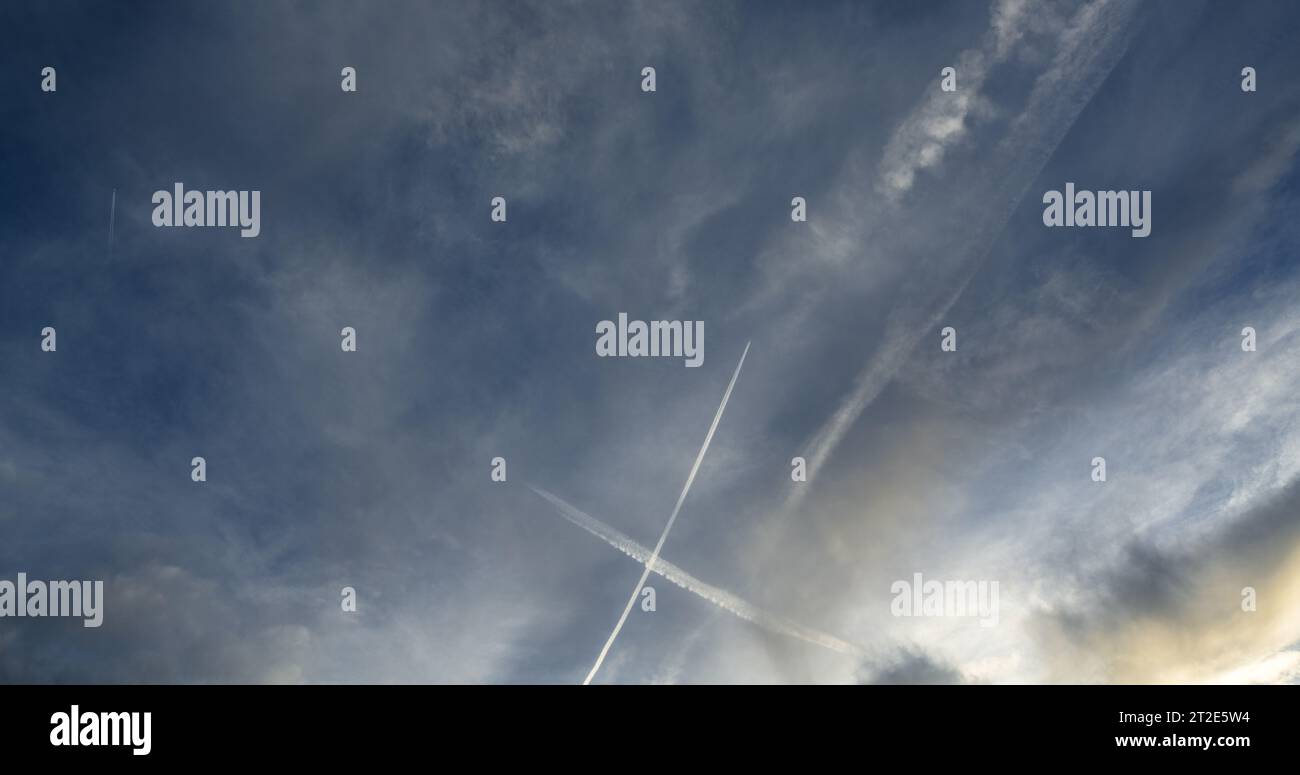 Gioco ipnotico di luce e ombra creato dalle piste di condensazione di un aereo di linea e dalle nuvole ad alta quota. Foto Stock