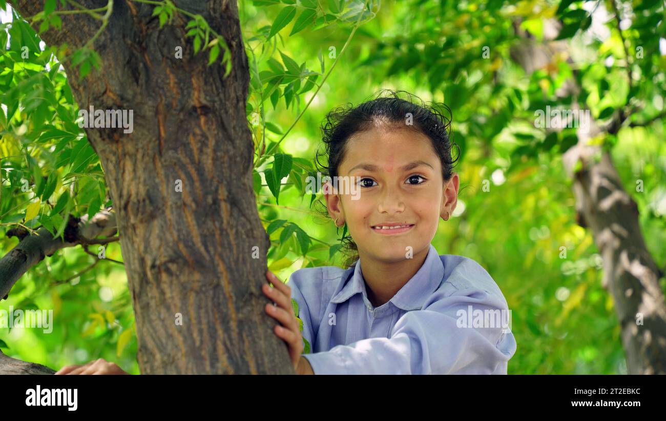 Felice ragazza sorridente appesa a un albero. Il bambino ride felicemente. Atmosfera primaverile. Stile di vita attivo. Arrampicata sugli alberi. Foto Stock