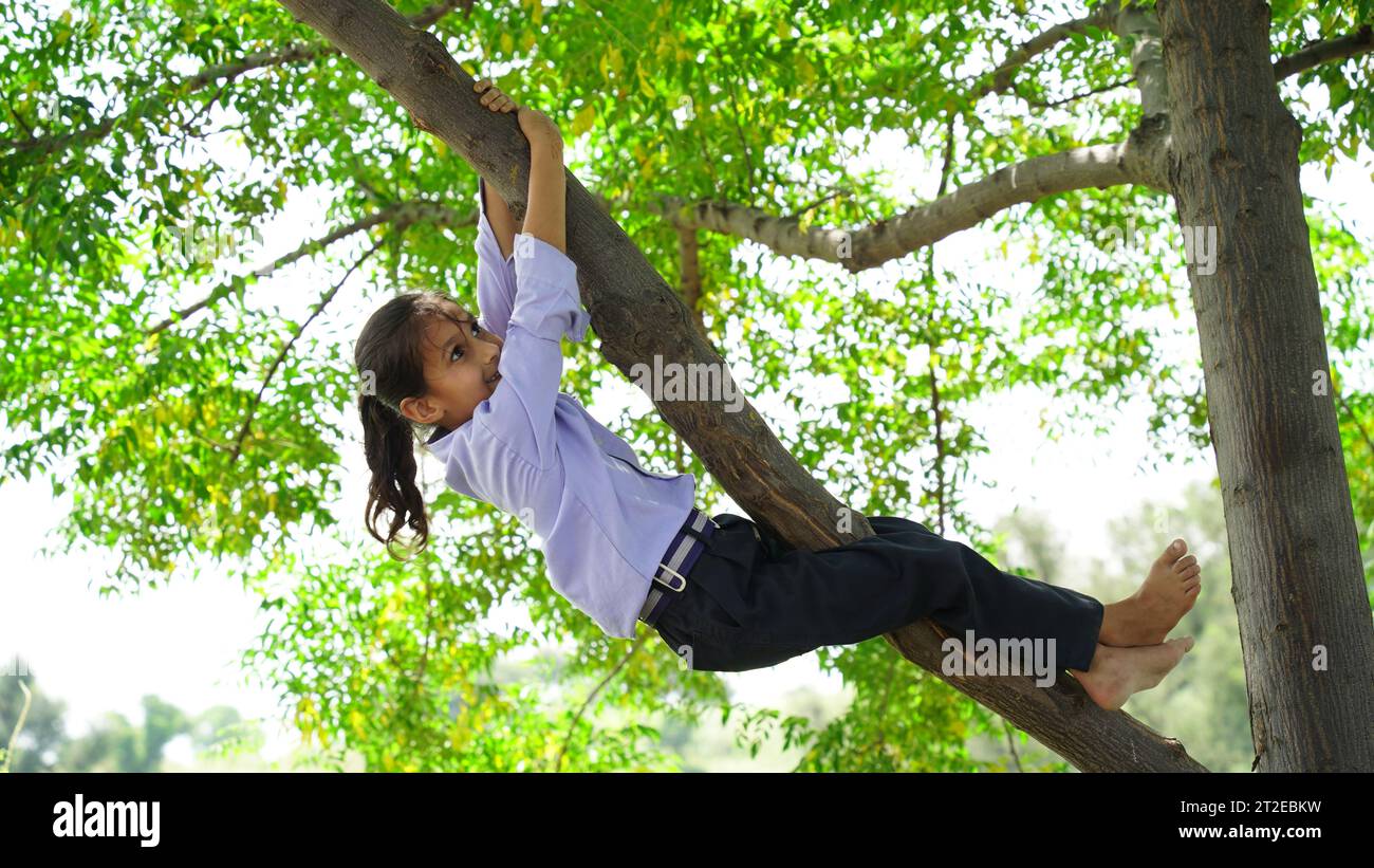 Felice ragazza sorridente appesa a un albero. Il bambino ride felicemente. Atmosfera primaverile. Stile di vita attivo. Arrampicata sugli alberi. Foto Stock