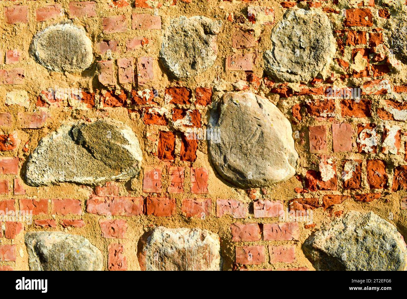 La consistenza dell'antica pietra medievale antica, il peeling duro, la parete di mattoni di argilla rossa rettangolare e grandi pietre, ciottoli. T Foto Stock