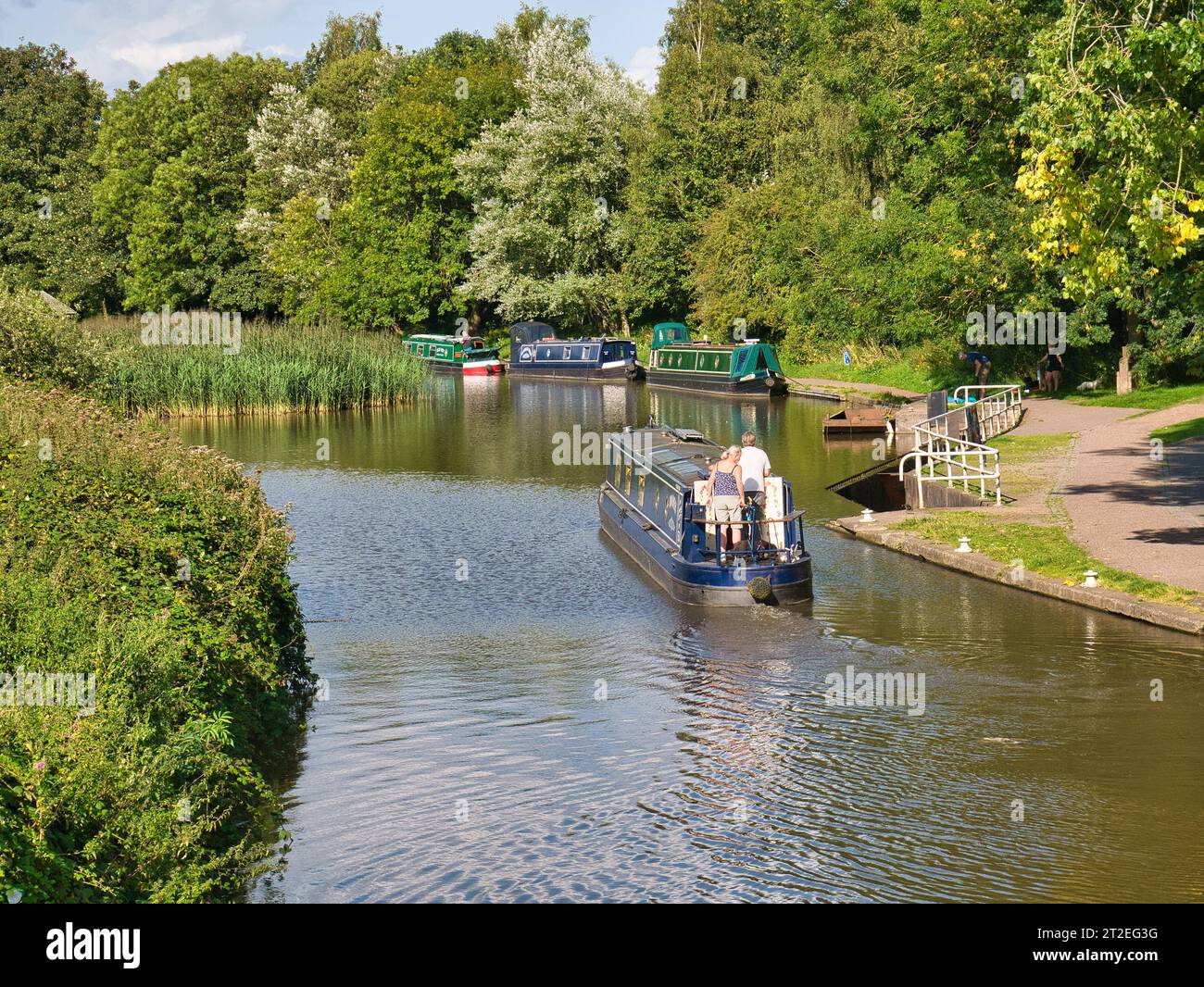 Un uomo e una donna a bordo di un narrowboat che naviga sul canale Trent e Mersey nel tranquillo e rurale Cheshire. In una giornata di sole d'estate. Foto Stock