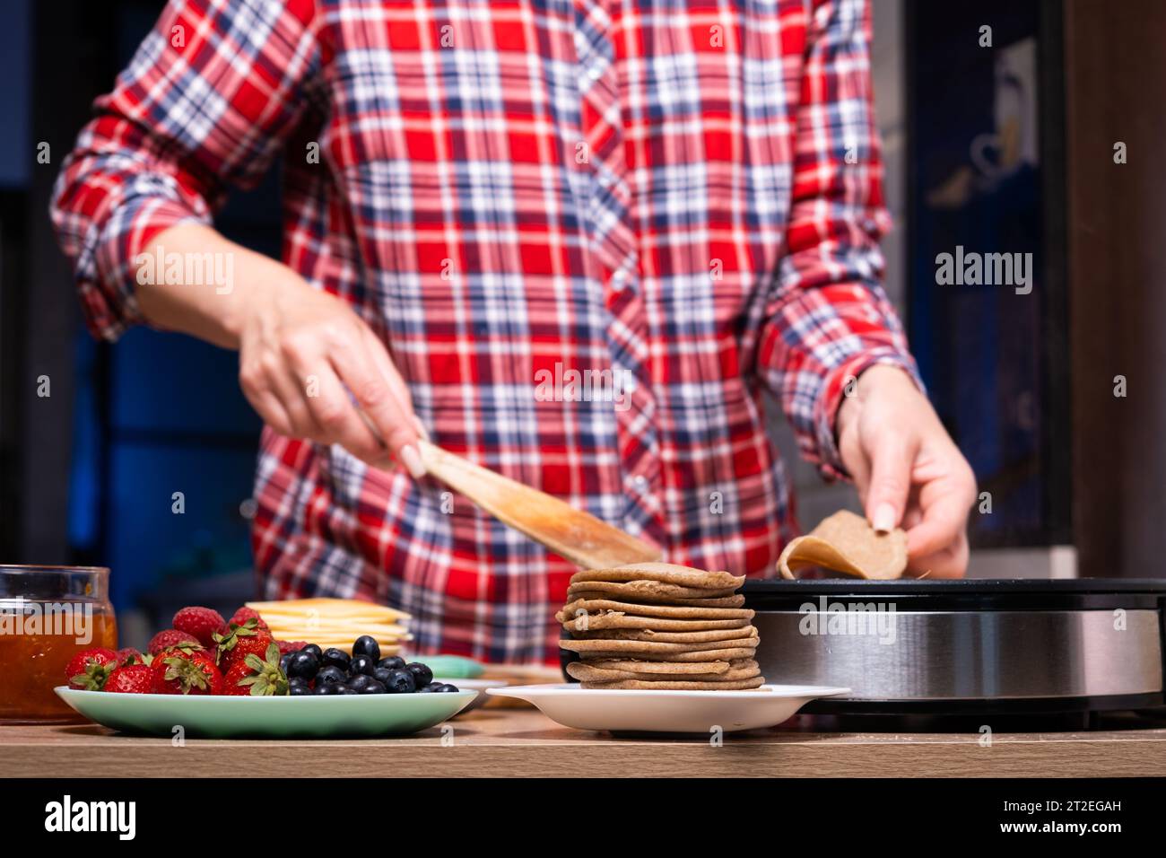 Donna che cucina deliziose crêpe sulla macchina per pancake elettrica in  primo piano della cucina