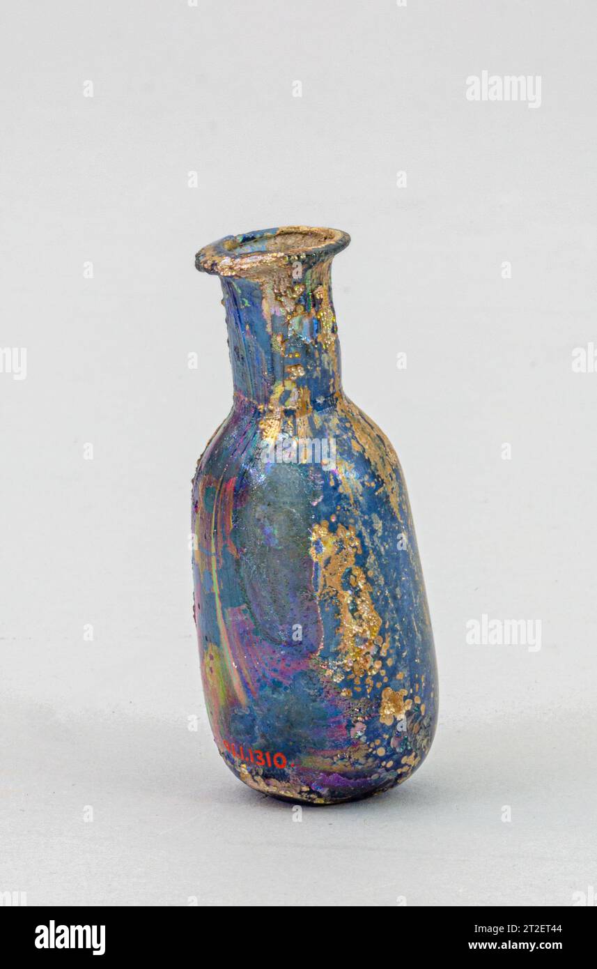 Bottiglia di profumo in vetro Roman i-III secolo CE blu traslucido. Bordo arrotolato, piegato sopra e dentro, con superficie superiore smussata; collo cilindrico, con segni di utensili orizzontali intorno alla base; spalla inclinata in modo ripido; corpo cilindrico, che si espande leggermente verso il basso; piccolo calcio al centro del fondo e grande contrassegno circolare del pontile.intatto; molte bolle e striature di soffiaggio; vaiolatura profonda e brillanti agenti atmosferici iridescenti. Visualizza altro. Bottiglia di profumo in vetro. Roman. I-III secolo. Vetro, soffiato. Imperial. Vetro Foto Stock