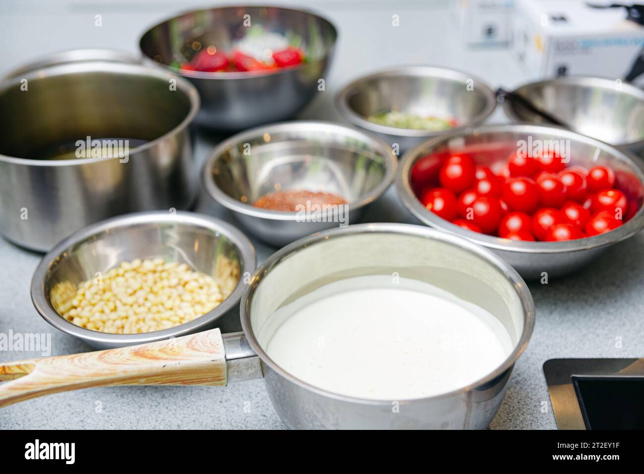set di ciotole e padelle in acciaio inox con prodotti crudi, pinoli, pomodori ciliegini, panna pesante in una barca con sugo di carne Foto Stock