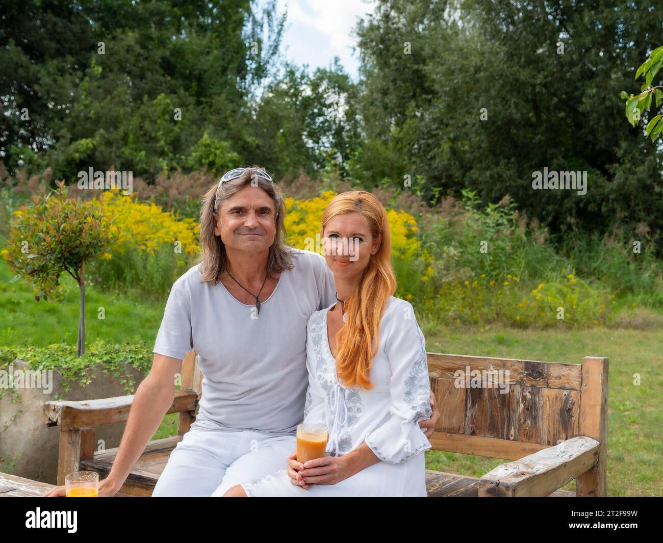 Uomo e donna in giardino su una panca da giardino, bevendo bicchieri con succo di frutta in mano, Germania Foto Stock