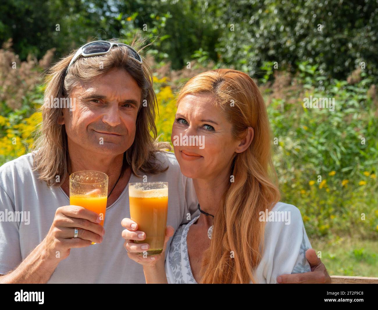 Uomo e donna in giardino con succo di frutta appena spremuto, coppia con bicchieri in mano che bevono, Germania Foto Stock