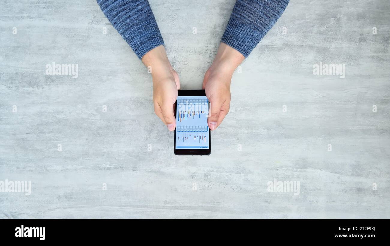 Vista dall'alto delle mani che reggono lo smartphone con grafici e dati. Concetto finanziario e commerciale. Foto Stock