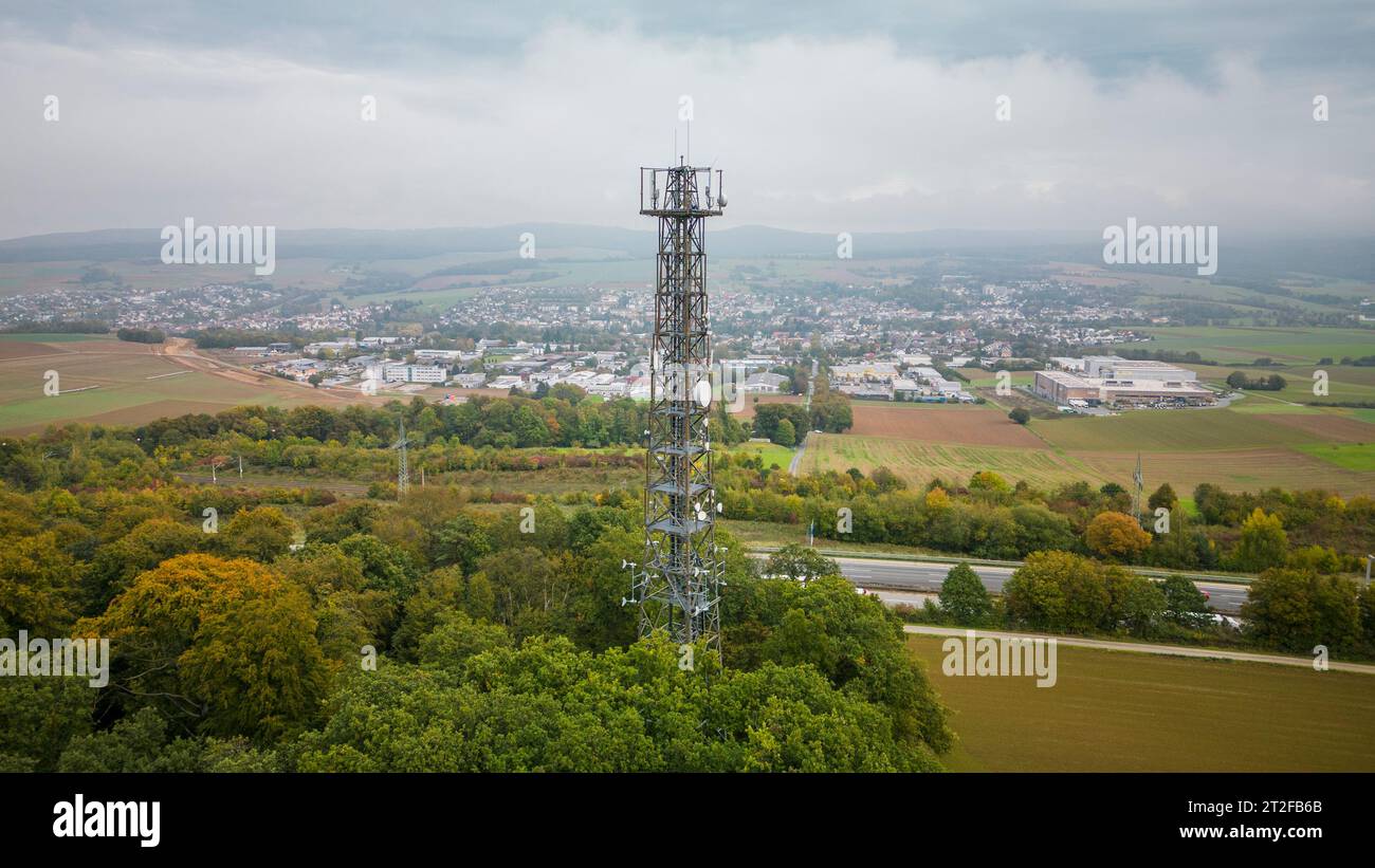 Bad Camberg, Germania. 20 ottobre 2023. La torre cellulare con turbine eoliche si trova direttamente sull'autostrada A3, con la città termale di Kneipp sullo sfondo. L'operatore di montante per telefono cellulare Vantage Towers, insieme alla Start-up di energia eolica MOWEA con sede a Berlino, ha commissionato il primo montante per telefono cellulare con micro turbine eoliche integrate in Assia. L'energia rinnovabile generata dalle turbine viene utilizzata direttamente in loco per far funzionare il sistema, che può coprire fino al 100% della domanda di energia elettrica in condizioni di vento medio. Credito: Andreas Arnold/dpa/Alamy Live News Foto Stock