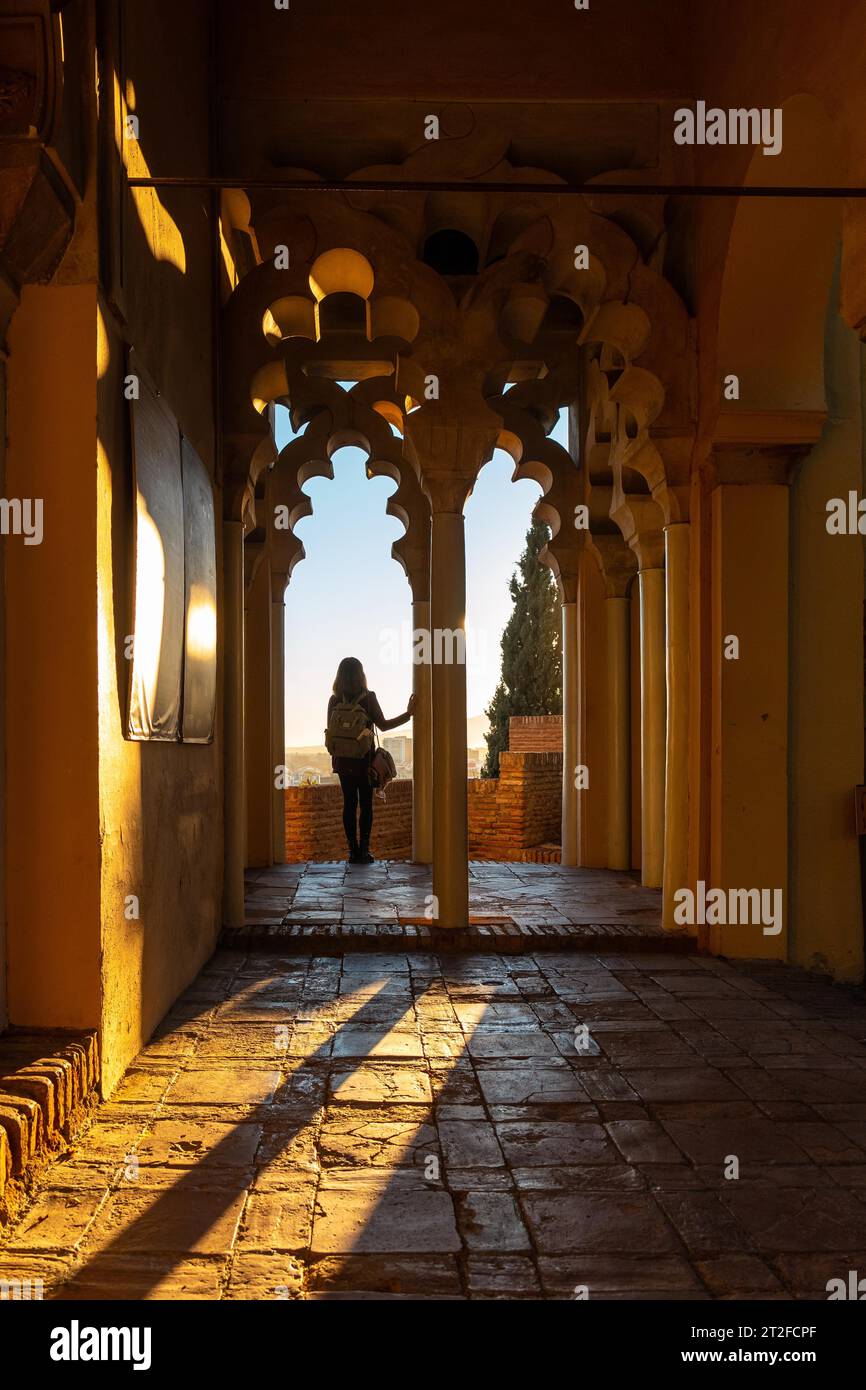 Una giovane donna al tramonto dalle porte arabe di un cortile dell'Alcazaba nella città di Malaga, Andalusia. Spagna. Fortezza medievale in stile arabo Foto Stock