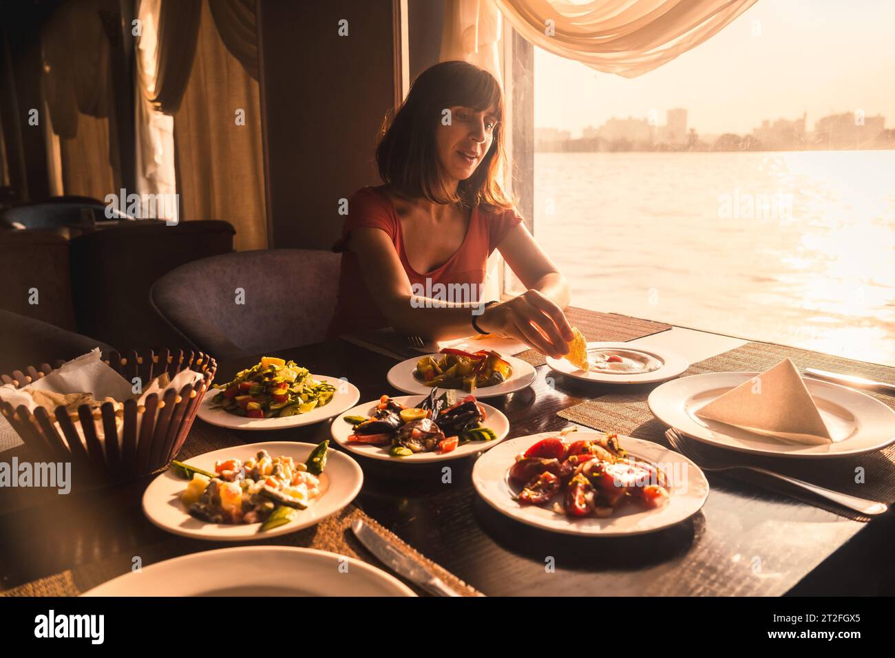 Un giovane turista che cena su una barca sul nilo un tradizionale pasto egiziano con la luce del tramonto nella finestra. Africa Foto Stock